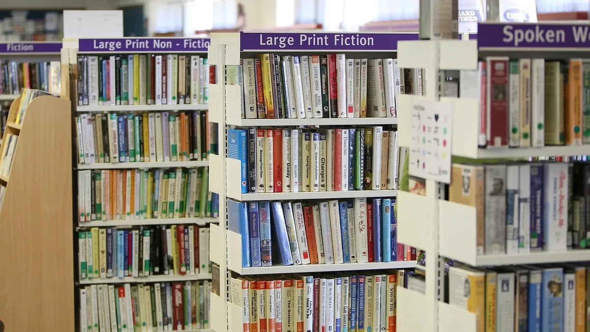 A section of a library with bookshelves containing large print fiction and non-fiction books, with a sign indicating a spoken word section.